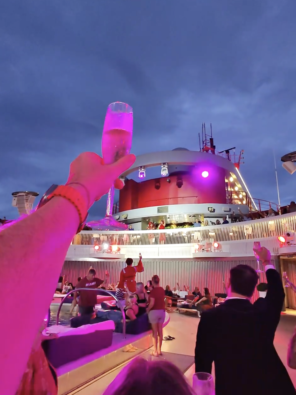 Raising a glass at the Virgin Voyages Sail Away party on the ship’s pool deck at sunset